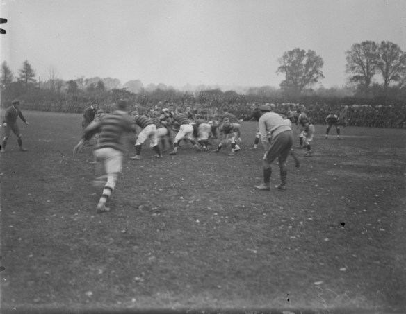 Photo noir et blanc de deux équipes de rugby en pleine mêlée. Deux arbitres surveillent la séquence de jeu.