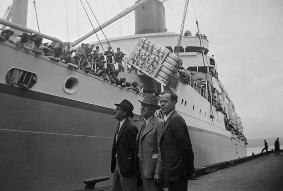 Photo noir et blanc de trois hommes debout devant un bateau.