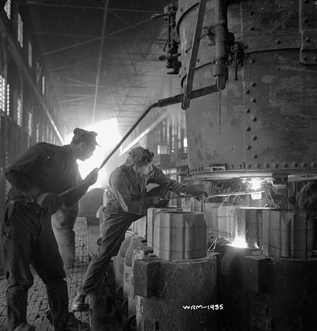 Photographie en noir et blanc d’ouvriers qui supervisent le coulage d’acier en fusion dans des moules.