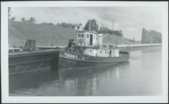 Photo noir et blanc d’un remorqueur à quai. L’équipage est sur le pont.