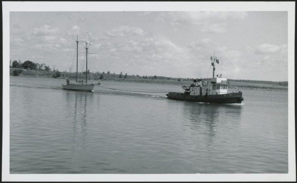 Photo noir et blanc d’un remorqueur tirant un voilier sur l’eau. 