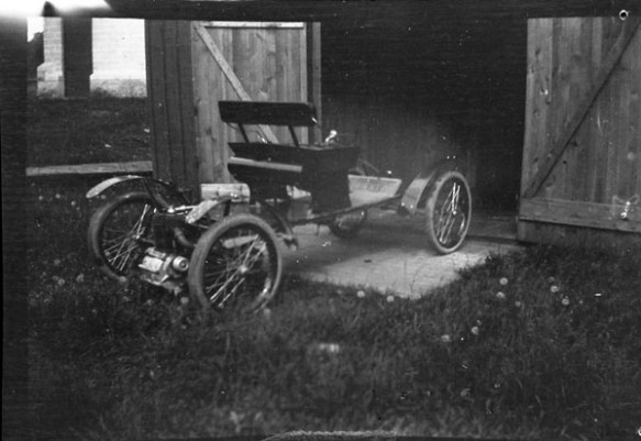 Photo noir et blanc d’une ancienne automobile garée à l’extérieur d’une grange.
