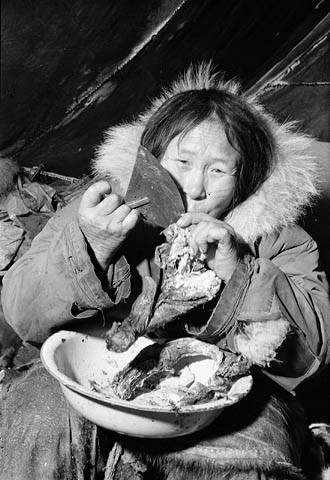 Photo noir et blanc d’une femme inuk se servant de son ulu pour trancher de la viande.