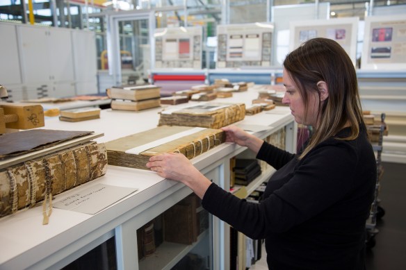 Photo couleur d’une personne se tenant debout devant une table dans le laboratoire de restauration des livres, réparant le dos d’un volume.