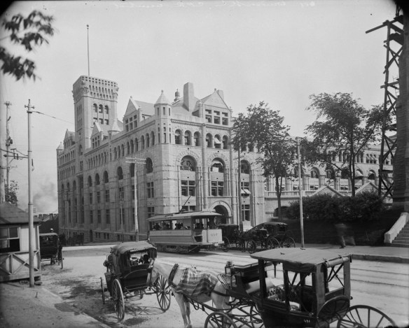 Photo noir et blanc d’un tramway, de chevaux et de calèches à l’extérieur de la gare Windsor, Montréal (Québec)