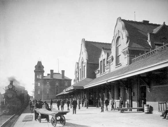 Photo noir et blanc de l’extérieur d’une gare du Chemin de fer Intercolonial; un train est arrêté sur la gauche et un groupe de personnes se tient sur le quai, Pictou (Nouvelle-Écosse)