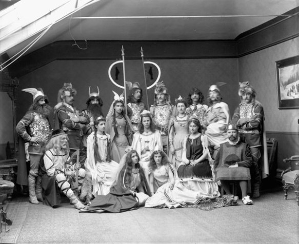 Photo noir et blanc d’un groupe de dix-sept hommes, femmes et filles vêtus de costumes de Vikings dans un studio de photographie.