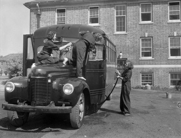 Photographie en noir et blanc de deux membres du Service féminin de la Marine royale du Canada qui lavent l’avant d’un autobus tandis que leur collègue en nettoie le côté avec un tuyau d’arrosage.