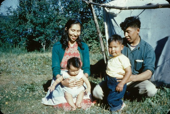 Un homme et une femme assis sur la pelouse avec deux jeunes enfants devant une tente en toile.