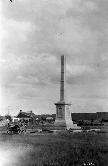 Photo en noir et blanc d’un obélisque avec un chariot sur roues à proximité.