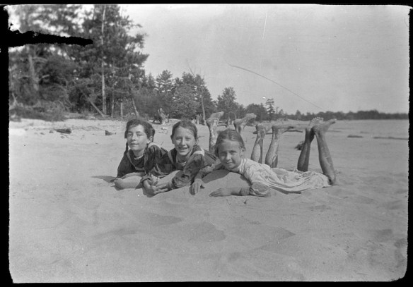 Photo noir et blanc de trois filles allongées côte à côte sur le ventre, dans le sable.