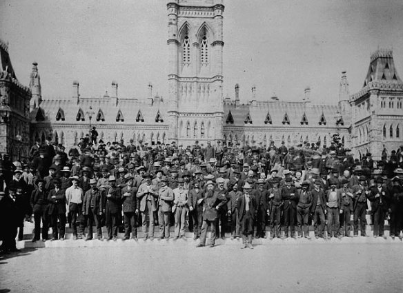 Photo noir et blanc d’un grand groupe d’hommes posant devant les édifices du Parlement.