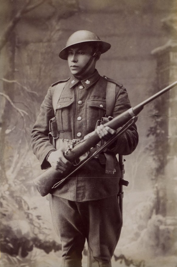 Portrait studio en noir et blanc d’un soldat de la Première Guerre mondiale, vêtu d’un uniforme, qui tient une carabine. 