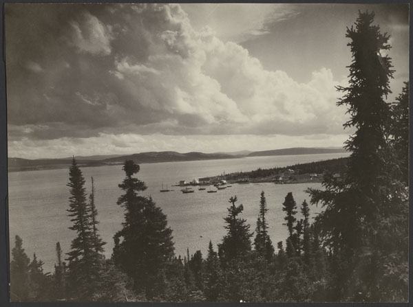 Photo noir et blanc de bateaux dans une baie. On voit des arbres à l’avant-plan.