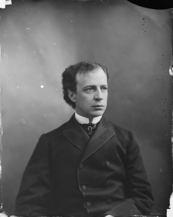 Photo noir et blanc d’un homme assis, vêtu d’un complet.