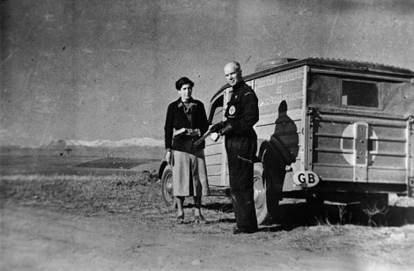 Photographie noir et blanc d’un homme et d’une femme debout devant une camionnette dont l’arrière est marqué d’une marqué d’une croix. 
