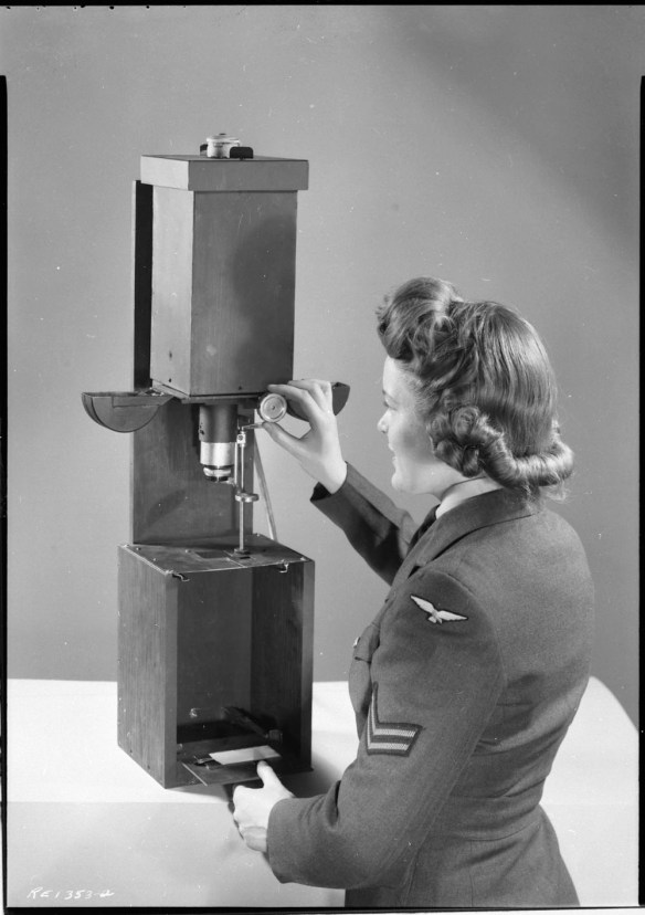 Photo noir et blanc d’une femme en uniforme militaire manipulant un agrandisseur.