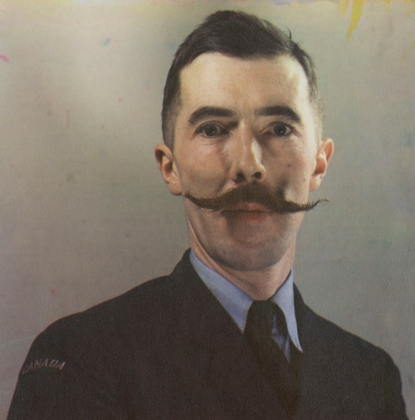 Autoportrait couleur de Brodie Macpherson en uniforme militaire arborant une moustache en guidon. Le sujet est représenté jusqu’à la poitrine devant un arrière-plan vierge.