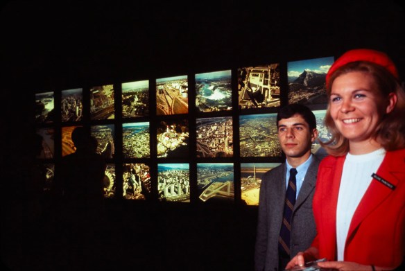 On aperçoit au premier plan une représentante de Kodak et un homme. On voit derrière eux des diapositives couleur rétroéclairées montrant des vues aériennes.