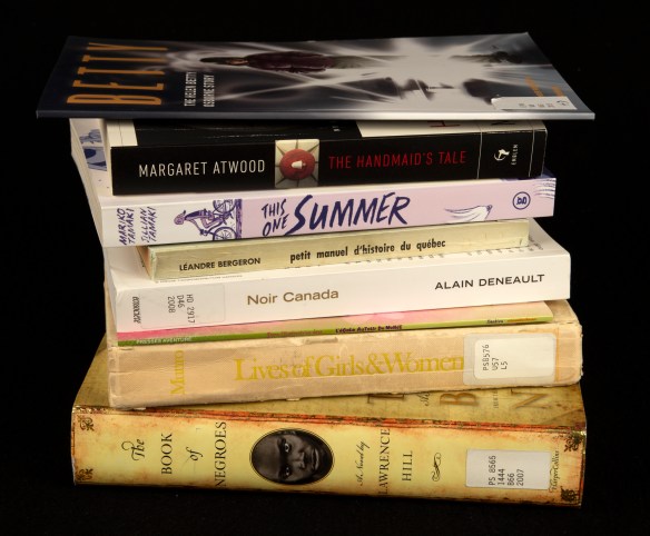 Photographie couleur montrant le dos de livres empilés sur fond noir.