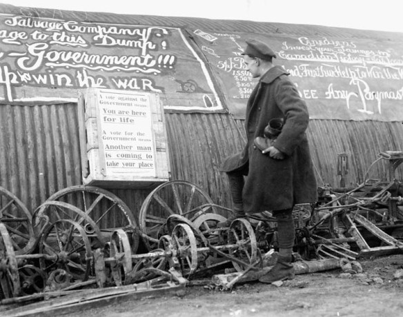 Photo noir et blanc d’un soldat en uniforme, lisant une affiche de propagande sur laquelle est écrit : « Un vote contre le gouvernement : vous restez ici pour toujours. Un vote pour le gouvernement : un autre homme prendra votre place ». [Traduction] 