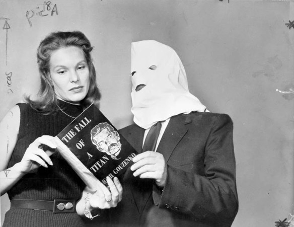 Photo noir et blanc d’une femme et d’un homme, une capuche lui recouvrant le visage, regardant un livre intitulé The Fall of a Titan. Sur la couverture, on voit une photo de Joseph Stalin et le nom de l’auteur, Igor Gouzenko.