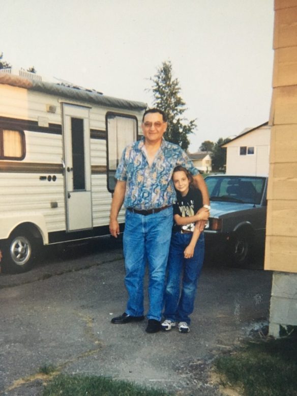 Photographie couleur d’un homme et d’une jeune fille souriants, posant devant une caravane blanche et une voiture.
