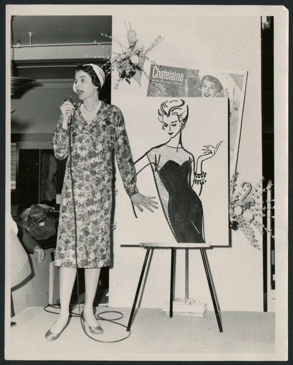 Photo noir et blanc montrant une femme qui parle au micro, devant un grand dessin de mode posé sur chevalet.