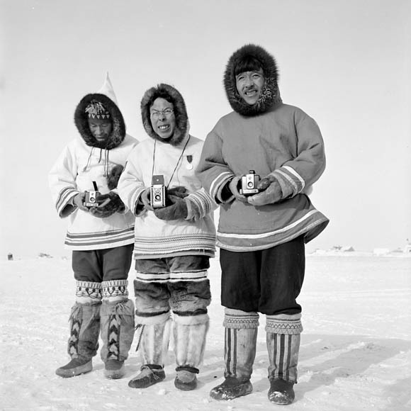 Photo noir et blanc de trois hommes inuit debout à l’extérieur pendant l’hiver. Ils portent tous des vêtements traditionnels.