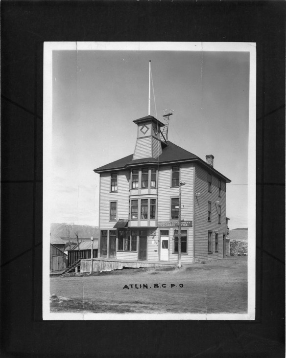 Photographie en noir et blanc du bureau de poste à trois étages d’Atlin, en Colombie-Britannique. Un panneau sur le bâtiment porte la mention « Dominion Government Telegraph Office ».