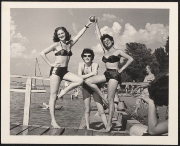 Photo noir et blanc de trois femmes en maillot de bain, prenant la pose sur un quai.