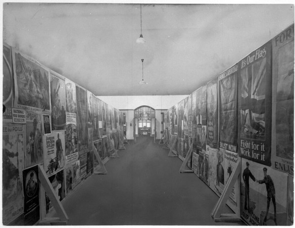 Photo noir et blanc d’une salle longue et étroite. Il y a deux luminaires suspendus au milieu de la salle, et les murs sont couverts d’affiches.