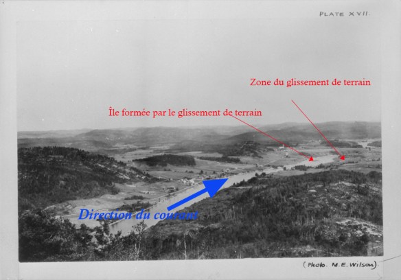 Une rivière bordée de maisons qui sillonne un paysage vallonné.