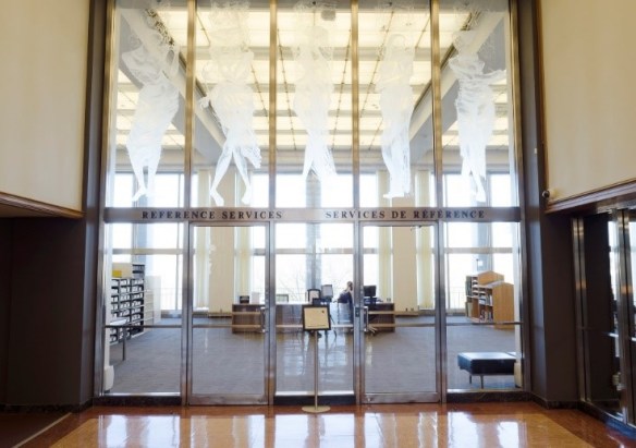 Photo couleur, prise depuis un corridor, d’une salle de référence que l’on voit à travers une paroi et deux portes vitrées.