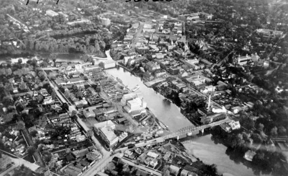 Une ville avec des maisons et des bâtiments de chaque côté d'une rivière, avec un pont reliant les deux côtés.